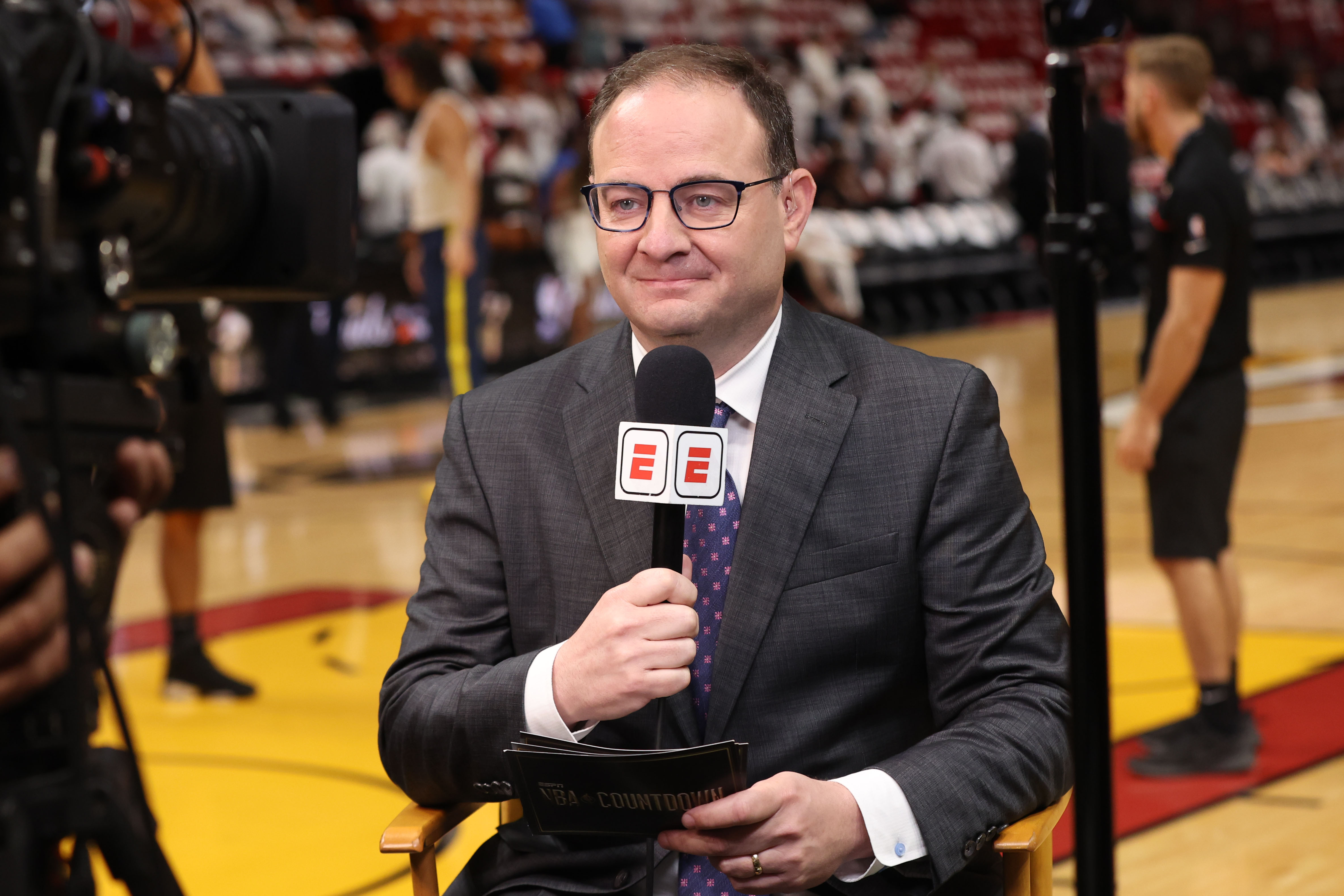 Adrian Wojnarowski sitting in a chair with an ESPN microphone. 