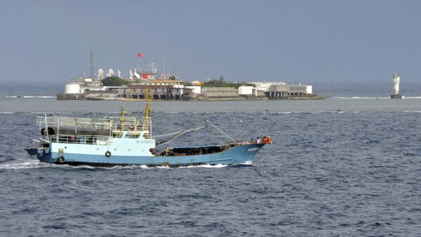 Chinese fishing vessel sails by Fiery Cross Reef, background, also known as Yongshu Reef, of the Spratly Islands in South China Sea. File photo. - Sputnik International