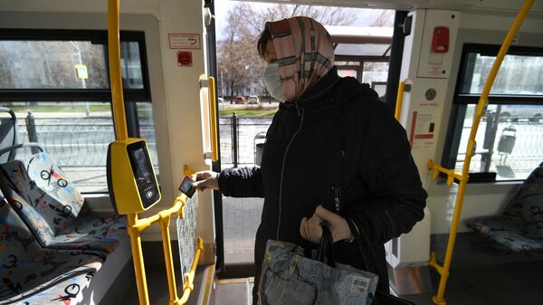 Женщина в защитной маске прикладывает социальную карту москвича к валидатору в салоне городского автобуса в Москве. 22 апреля 2020