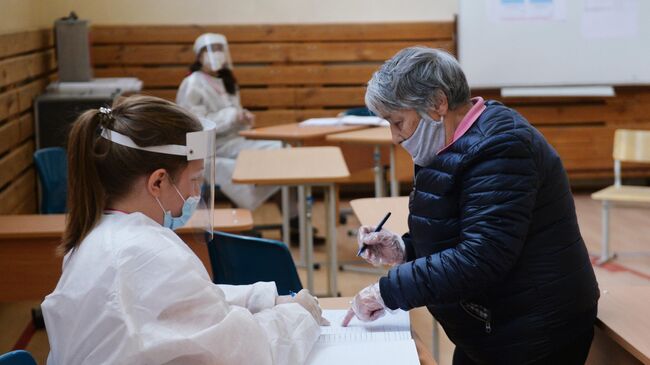 Женщина отмечается в списке избирателей на избирательном участке во время голосования по одобрению внесения поправок в Конституцию РФ