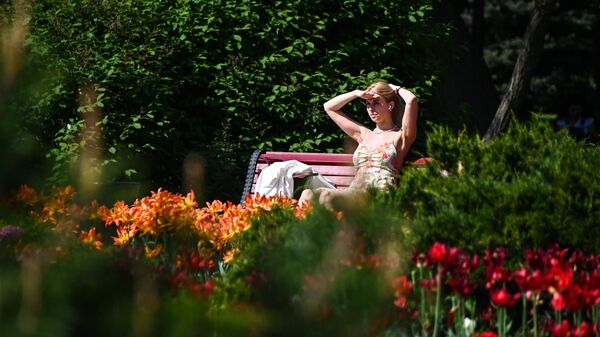 Девушка отдыхает под солнцем на скамейке в парке в Москве в жаркую погоду