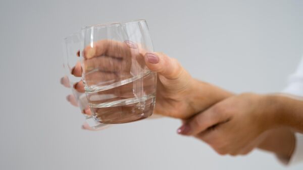 Женщина с болезнью Паркинсона держит стакан с водой