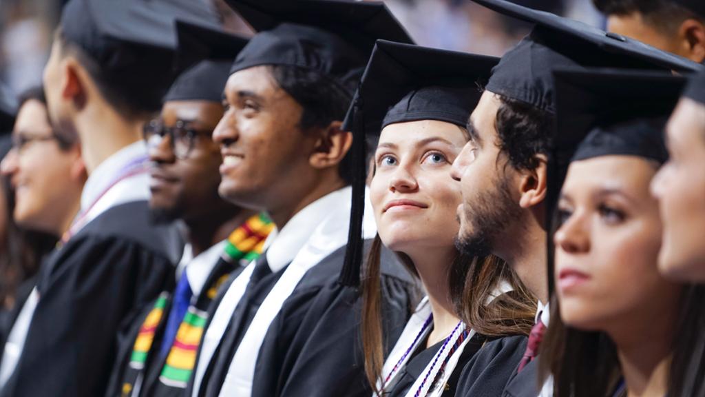 A row of graduating students in caps and gown sitting proudly at commencement.