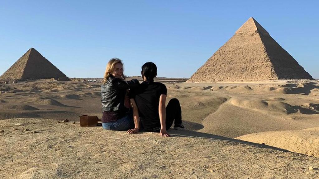 Two students sitting on the sand in Egypt in front of the pyramids.