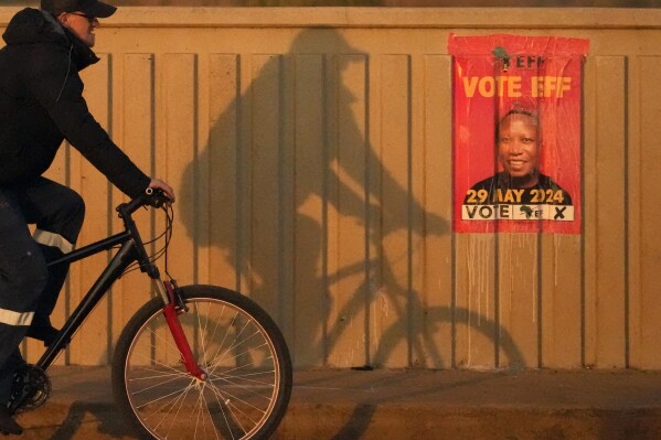 A man cycles past an Economic Freedom Fighters (EFF) poster with the face of its leader Julius Malema, in Benoni, east of Johannesburg, South Africa, Monday, May 27, 2024. South Africans who received special permission to vote early were casting their ballots on Monday, ahead of main elections on Wednesday, May, 29, 2024. (AP Photo/Themba Hadebe)