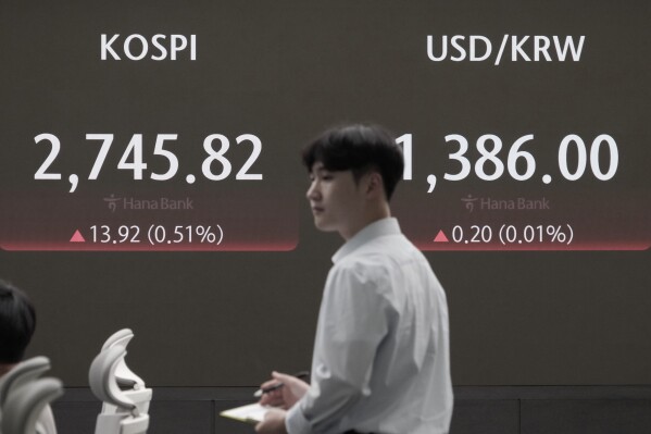 A currency trader passes by the screen showing the Korea Composite Stock Price Index (KOSPI), left, and the foreign exchange rate between U.S. dollar and South Korean won at the foreign exchange dealing room of the KEB Hana Bank headquarters in Seoul, South Korea, Monday, July 29, 2024. (AP Photo/Ahn Young-joon)
