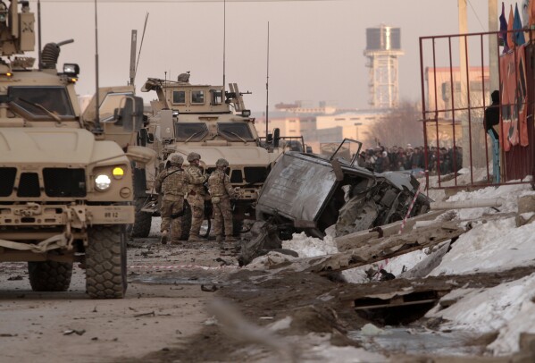 FILE - U.S. soldiers and Afghan security forces search the site where a suicide attacker rammed a car bomb into a NATO convoy killing two foreign civilian contractors, in the Afghan capital Kabul, Afghanistan, Feb. 10, 2014. (AP Photo/Rahmat Gul, File)