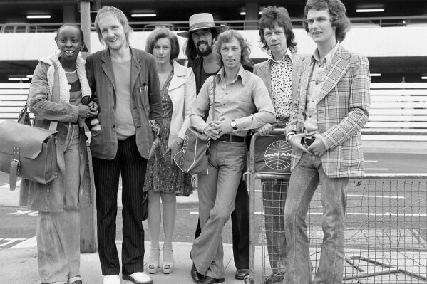 FILE - The Blue Mink pop group including Roger Cook, wearing hat, Madeline Bell, left, and bass player Herbie Flowers, second right, leaving London for Los Angeles, and the start of a two week tour on July 1973. Flowers, who played with David Bowie, Elton John, Lou Reed and other music legends in a decades-long career, has died at 86. (PA via AP, File)