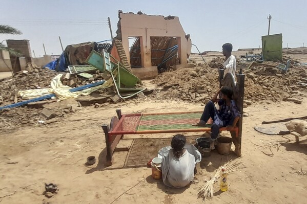 People sit in front of their home damaged by floods in Meroe, north of Khartoum, Sudan, Tuesday, Aug. 20, 2024. (AP Photo/Marwan Ali)