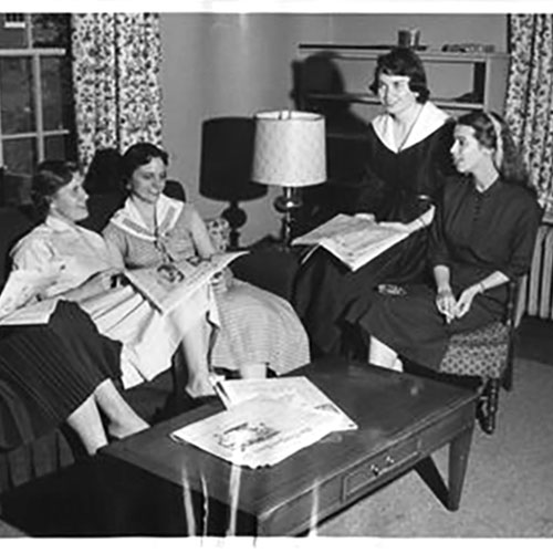 A black and white photograph shows Edward R. Murrow sitting in an easy chair in profile to the camera. He is reading a newspaper.