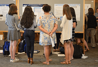 Several people gathered around poster of student research project results