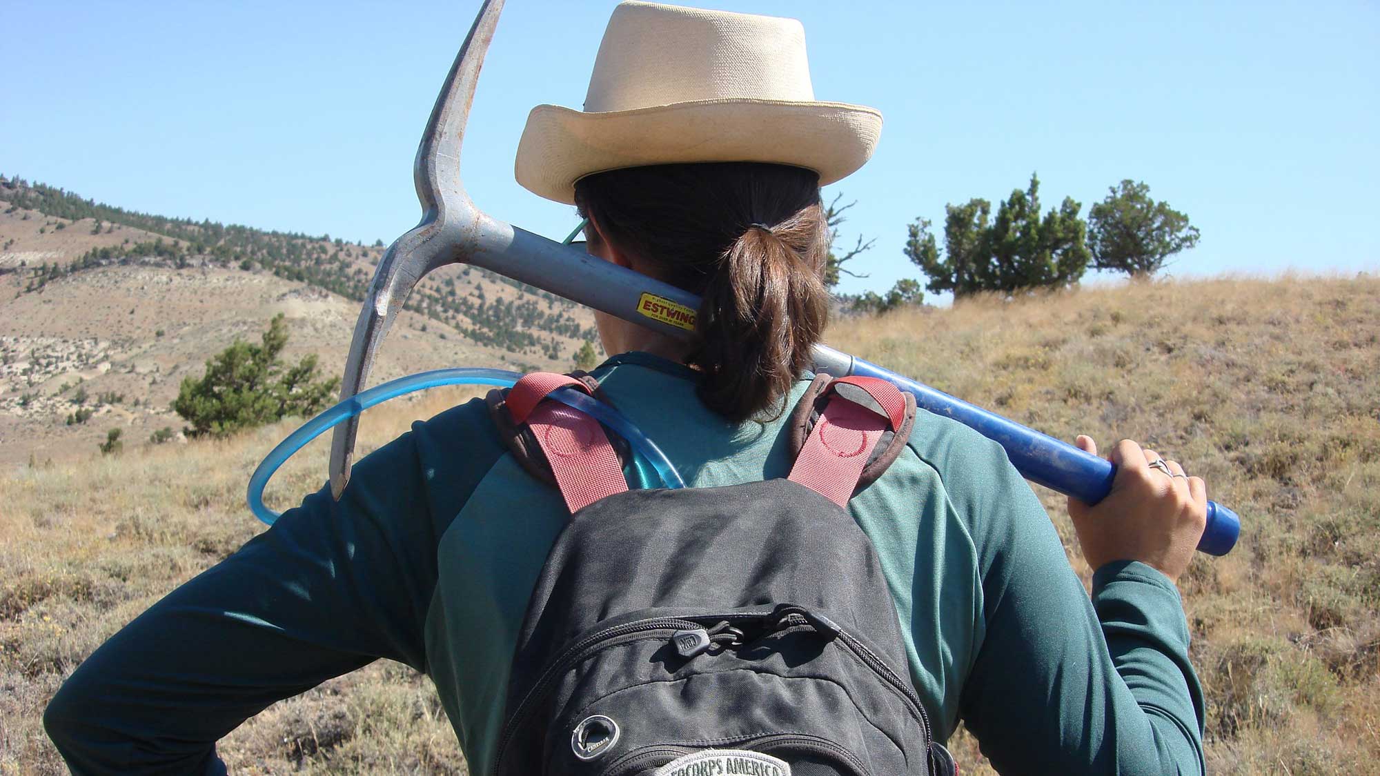 Photograph of a geologist holding a pick and looking at some hills.