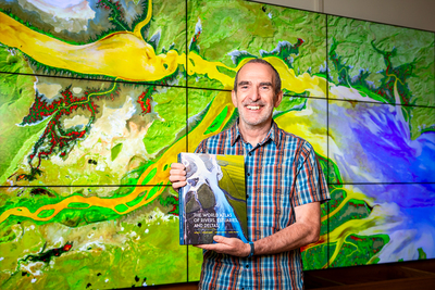 Researcher Jim Best standing in front of a project of one of the satellite image from his new atlas.