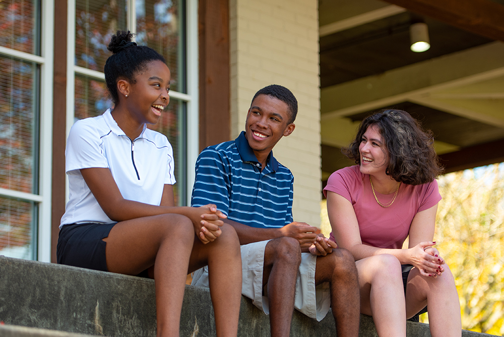 Three First Tee participants talking and laughing outside.