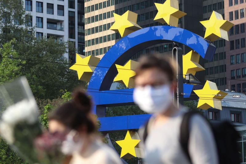 People wearing face masks walk in front of a euro sign in Frankfurt am Main, Germany, on April, 24.