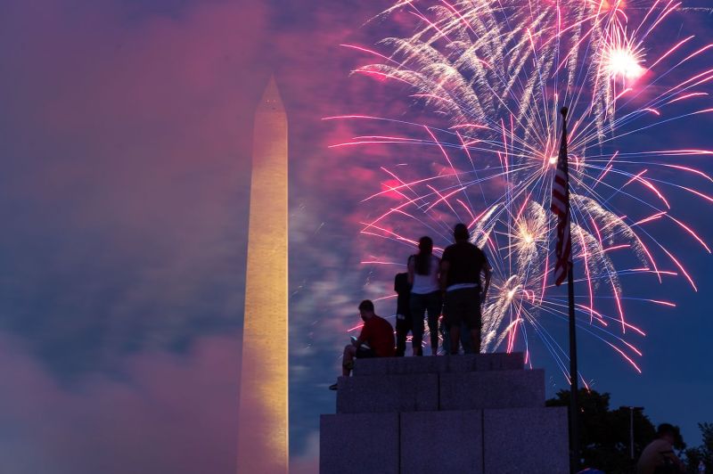 Spectators sit on top of a pillar at the World War II Memorial in the National Mall as fireworks explode in Washington, D.C., on July 4.
