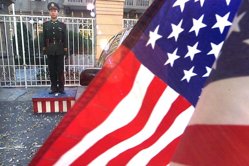 A PLA soldier stands guard beside a U.S. flag outside World Trade Organization talks in Beijing in 1999.