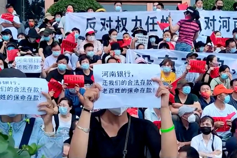 In this screengrab from video obtained by Reuters, demonstrators hold up signs during a protest over the freezing of deposits by some rural-based banks outside a People's Bank of China building in Zhengzhou, Henan province, China, on July 10. Text in foreground reads, "Henan Bank, return to us our legal deposits! The people's life-saving deposits!"