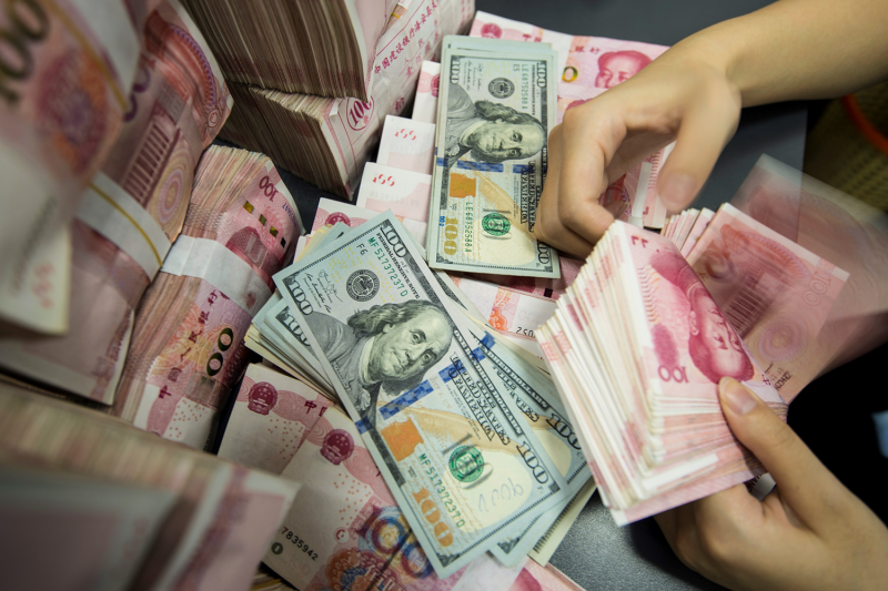 A Chinese bank employee counts 100-yuan notes and U.S. dollar bills