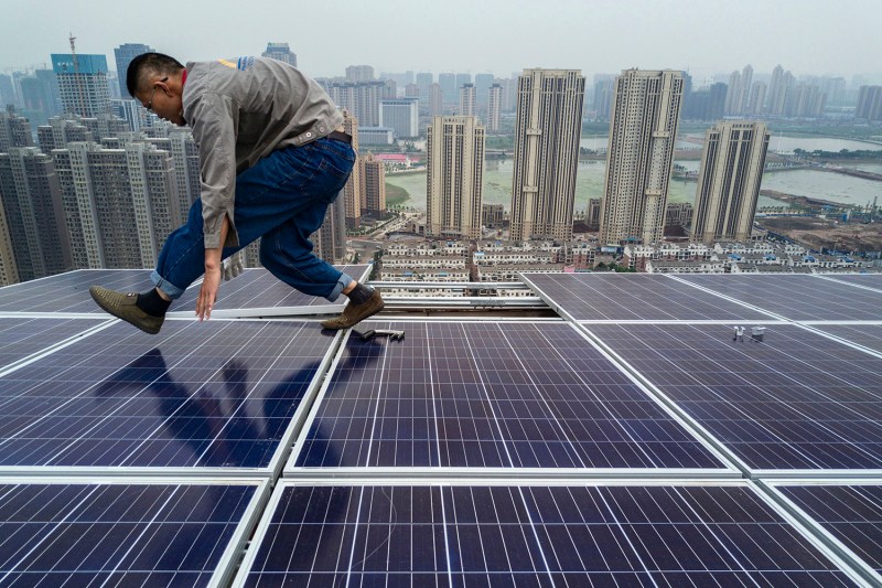 A worker stands atop a solar panel during construction on the roof of a new development in Wuhan. Buildings can be seen in the background.