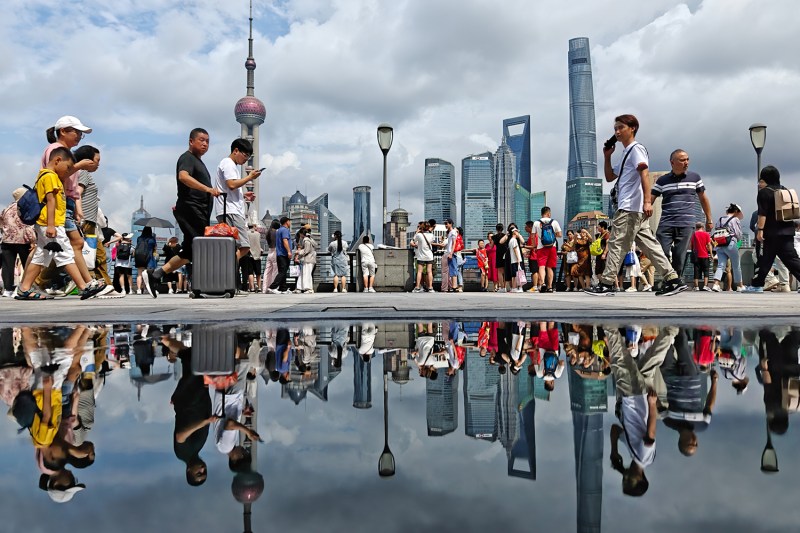 People walk along Shanghai's Bund waterfront with skyscrapers of the Lujiazui financial district in the background.