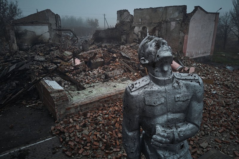 A crumbling, damaged statue of a Soviet soldier in uniform is seen against the brick and metal rubble of a house of culture that was destroyed by rocket fire in Ukraine.