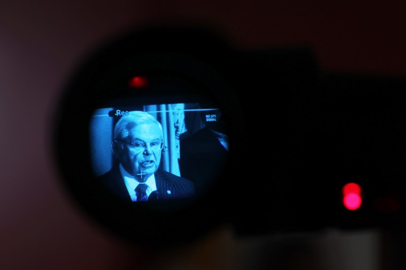 U.S. Sen. Bob Menendez is seen in a circle inside the viewfinder of a camera as he speaks during a news conference. A blurry red recording light is seen to the right.