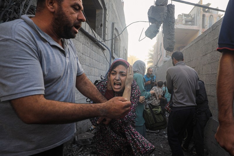 A young woman wearing a headscarf screams and presses her hands to her face as she and others flee through the rubble during Israeli airstrikes on al-Maghazi refugee camp in the central Gaza Strip.