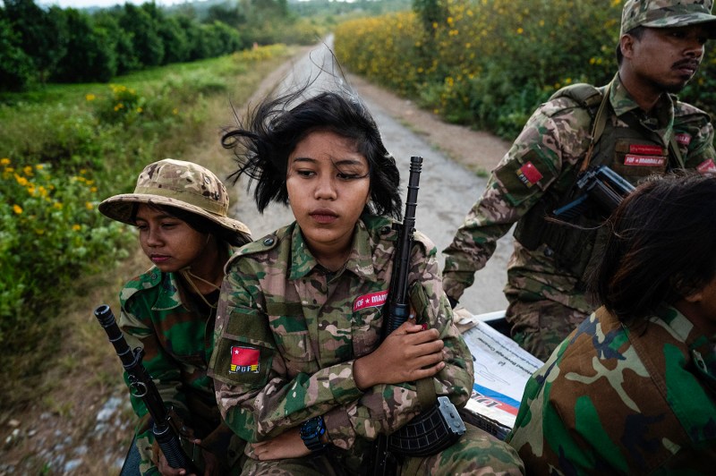 Members of the Mandalay People's Defense Forces, wearing camouflage and holding guns, head to the frontline down a road lined with greenery and flowers amid clashes with the Myanmar military.