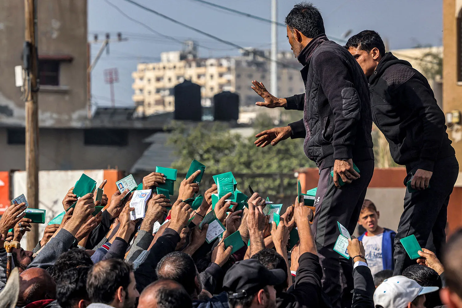 A large group of Palestinians wave identity cards as they gather to receive rations.
