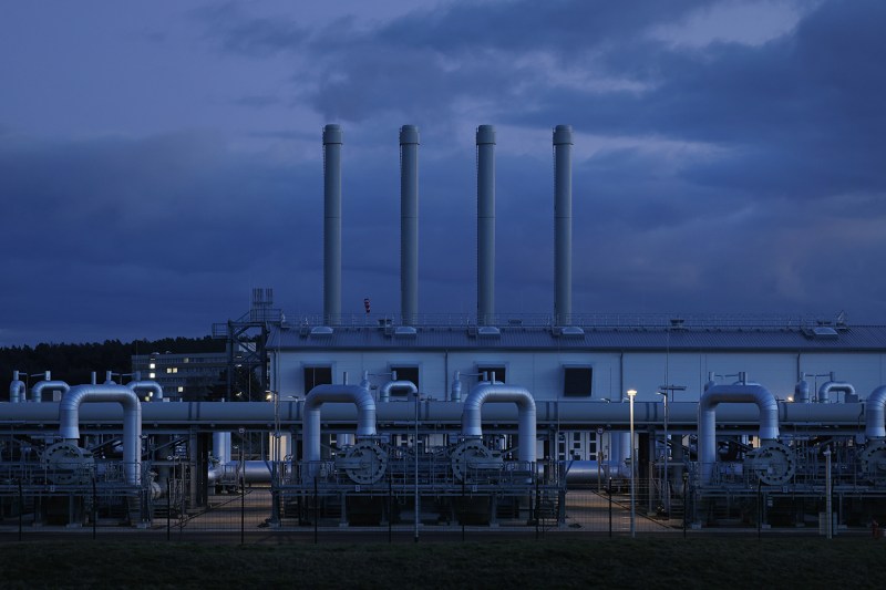 Four exhaust pipe towers from a gas pipeline station release smoke into the twilight sky.