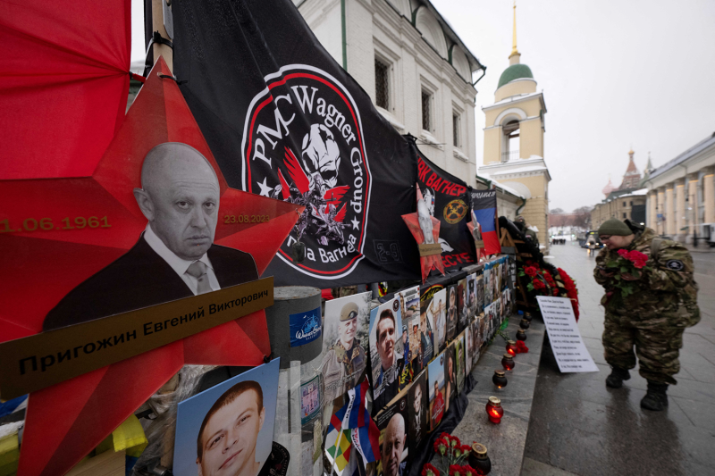 Soldiers wearing camouflage fatigues visit a makeshift memorial for Wagner Group leader Yevgeny Prigozhin in Moscow. The informal memorial is on the side of a street and is covered with flags, photos of Prigozhin, and candles.