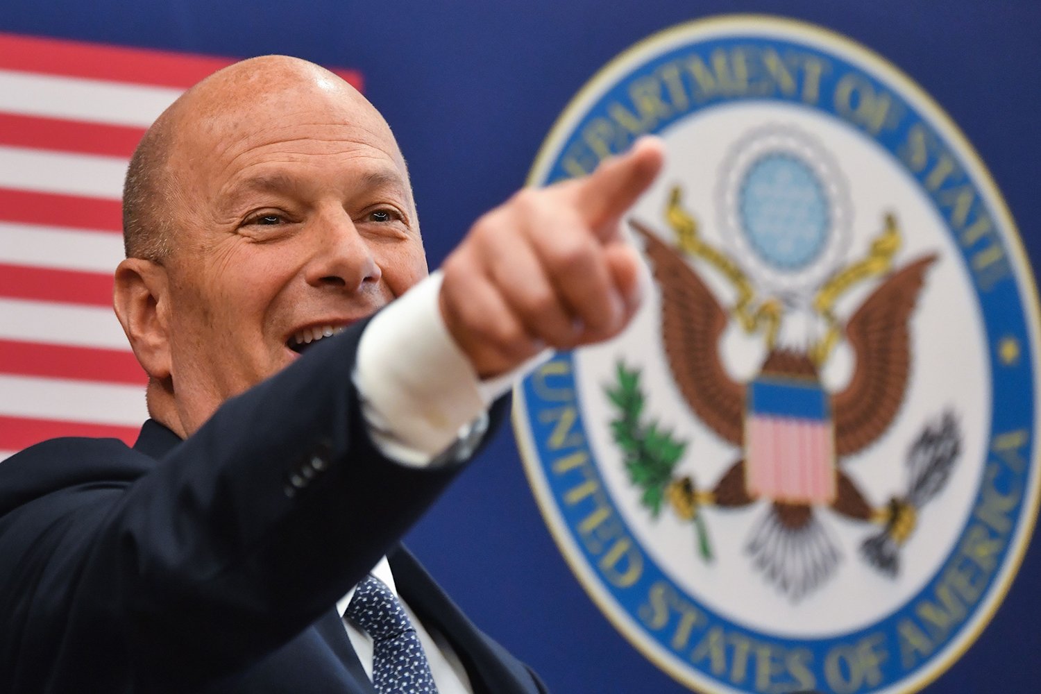 Gordon Sondland points the audience in front of an American flag and the presidential seal.