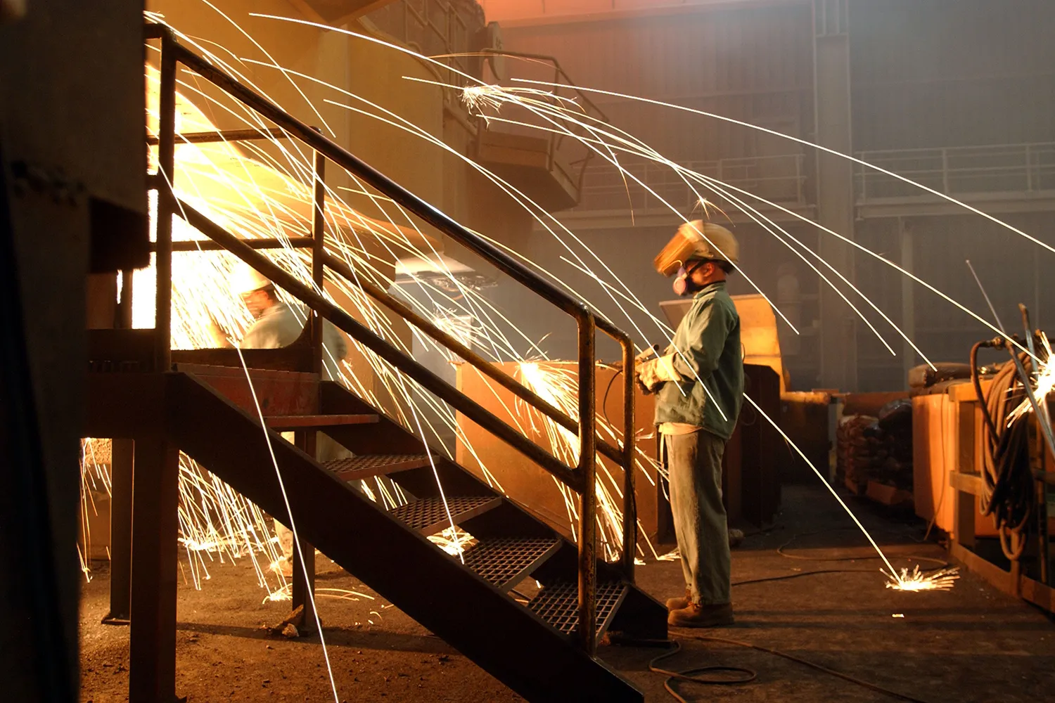 A worker is surrounded by sparks from molten steel in a factory.