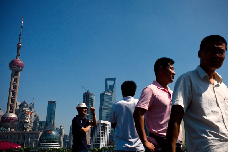 Four men in short-sleeved polo or button-up shirts walk past the skyline of Shanghai.