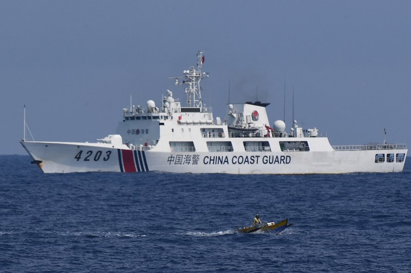 A China Coast Guard ship monitors a Philippine fisherman aboard his wooden boat in the South China Sea.