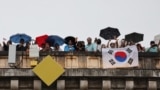 Penonton dengan bendera Korea Selatan menyaksikan parade apung di Sungai Seine dari jembatan Paris selama upacara pembukaan Olimpiade, 26 Juli 2024. (Foto: AFP)
