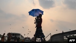 ရာသီဥတု ပူးပြင်းလွန်းလို့ ရန်ကုန်မြို့မှာ ထီးရိပ်ခို လမ်းလျှောက်နေသူတဦး။ (AFP)