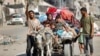 A man gestures while leading a donkey pulling a cart transporting his family members and belongings as they try to return to their home in the Tuffah district east of Gaza City, July 8, 2024. 