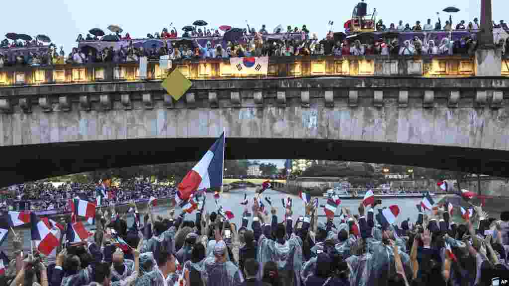 French athletes wave flags as they travel by boat on the Seine river during the opening ceremony of the 2024 Summer Olympics in Paris, July 26, 2024.