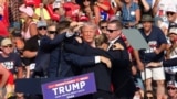 Агенты Секретной службы уводят бывшего президента США Дональда Трампа со сцены после того, как было совершено покушение на его убийство во время предвыборного митинга в г. Батлер (Пеннсильвания).