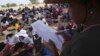 FILE - A woman reads out names of people waiting to receive food during a food distribution in Mangwe district southwestern Zimbabwe, amid a severe drought in Zimbabwe, March, 22, 2024.