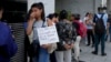 2024年2月5日一名婦女在阿根廷人力資本部長辦公室外與其他人一起排隊等待援助。標語牌上面西班牙文寫著：「我是貝蒂，一名學生，我沒有足夠的食物」。