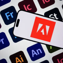 Adobe logo on a smartphone screen against the backdrop of Adobe program logos 