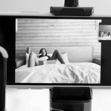 An iPhone sits on a tripod, filming a woman who lays with her legs open on a bed.