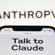 Anthropic Claude website displayed on a phone screen and Anthropic logo displayed on a screen in the background