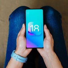 ios 18 logo on a smartphone being held in someone's hands on their lap