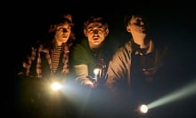 In "Stranger Things: The First Shadow" three teens with flashlights look scared.
