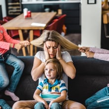 Small kids spending time with their frustrated nanny at home. Little girls are having fun while pulling her hair.