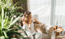 Woman sitting in arm chair with book and a cup of tea in a cozy, sunny room